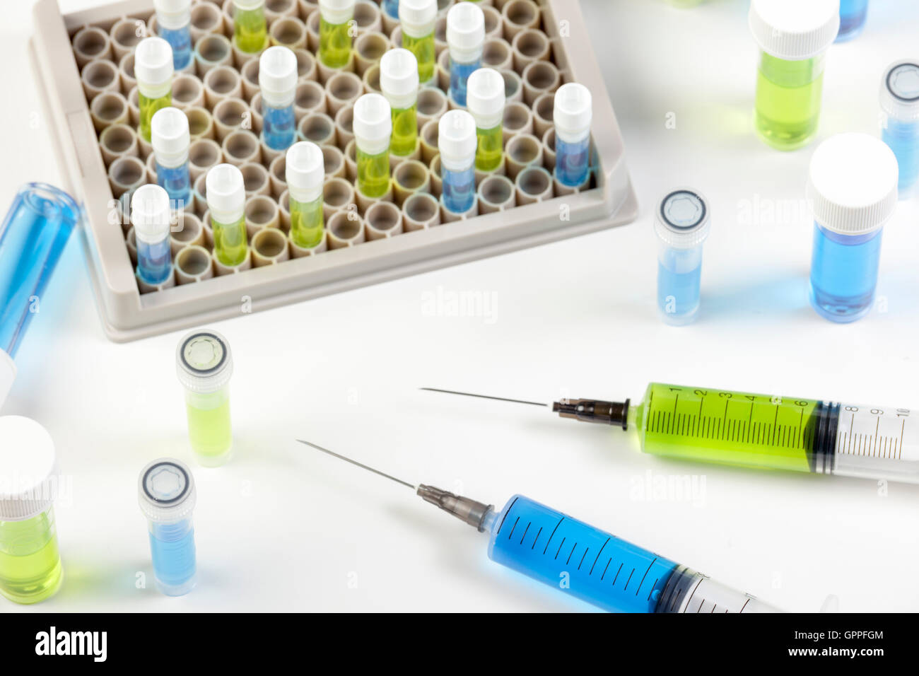 La siringa e fiale riempite con il verde e il blu fluidi su un laboratorio di bianco sul banco di lavoro Foto Stock