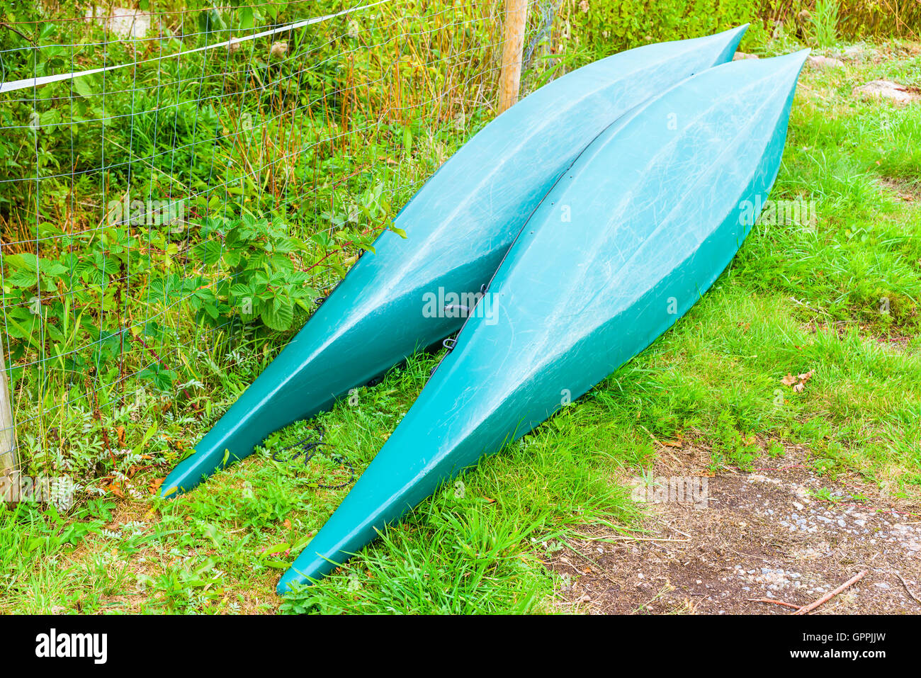 Due capovolto plastica canoe o kayak sulla terra asciutta. Le canoe sono verdi e lye accanto a un recinto reticolare accanto a una stretta walkwa Foto Stock