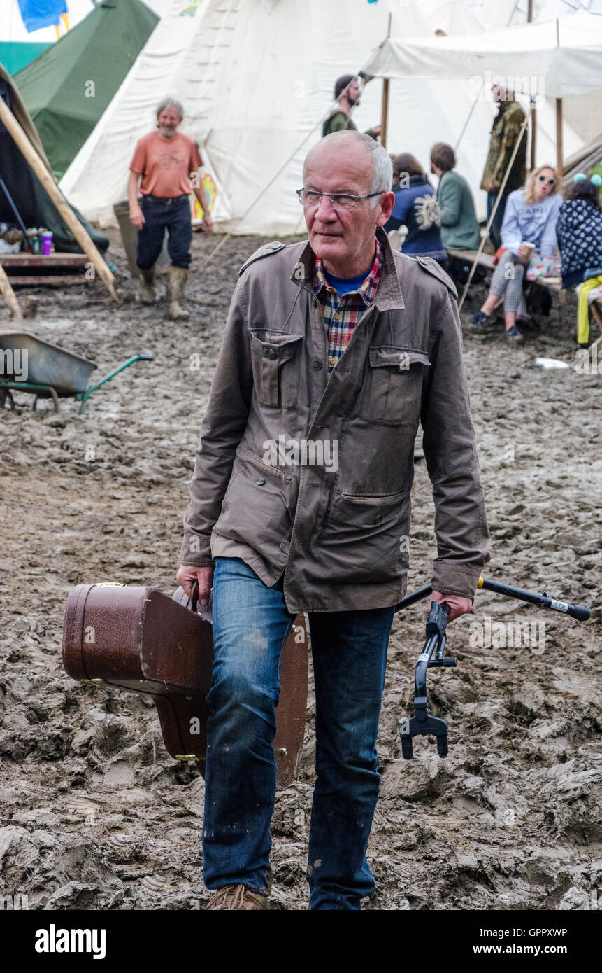 Un festival-goer portando una chitarra trudges attraverso il fango al Glastonbury festival Foto Stock