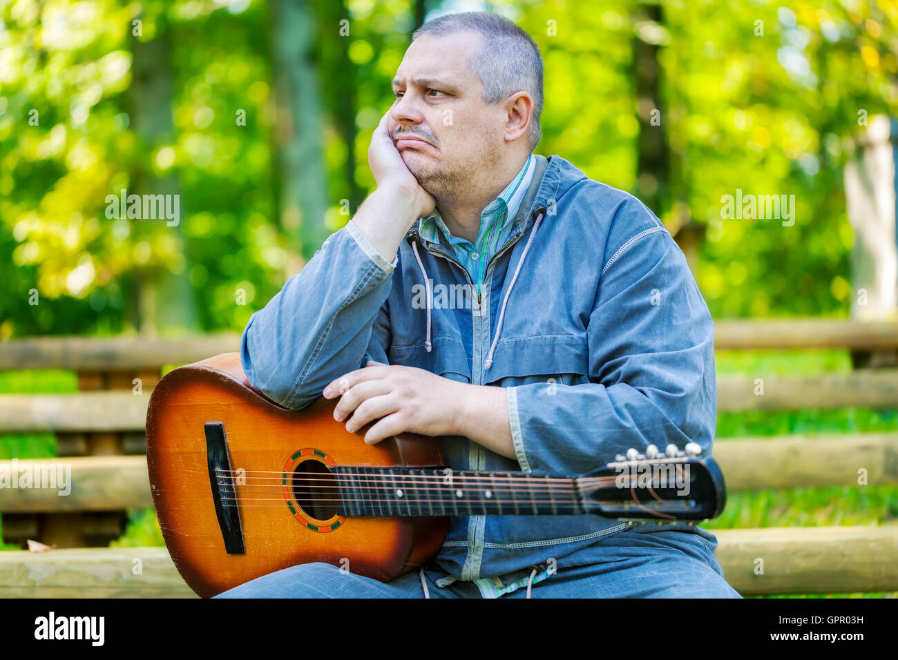 Triste uomo con chitarra in park sul banco di lavoro Foto Stock