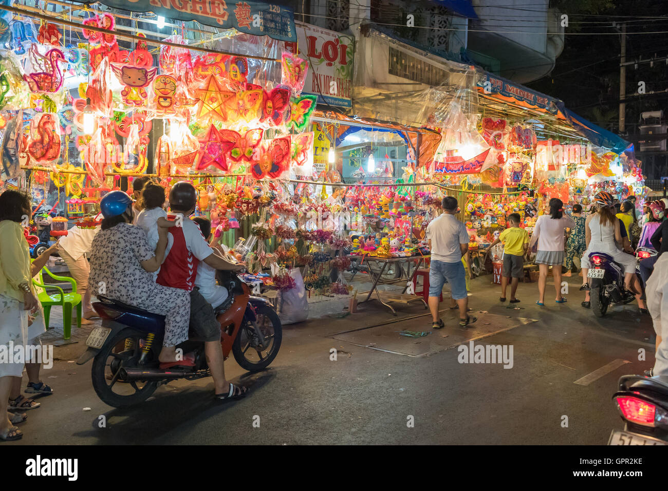 Motocicli guida nella parte anteriore di lanterne e giocattoli sorge nelle strade di Cholon a Ho Chi Minh City Vietnam durante metà autunno Foto Stock