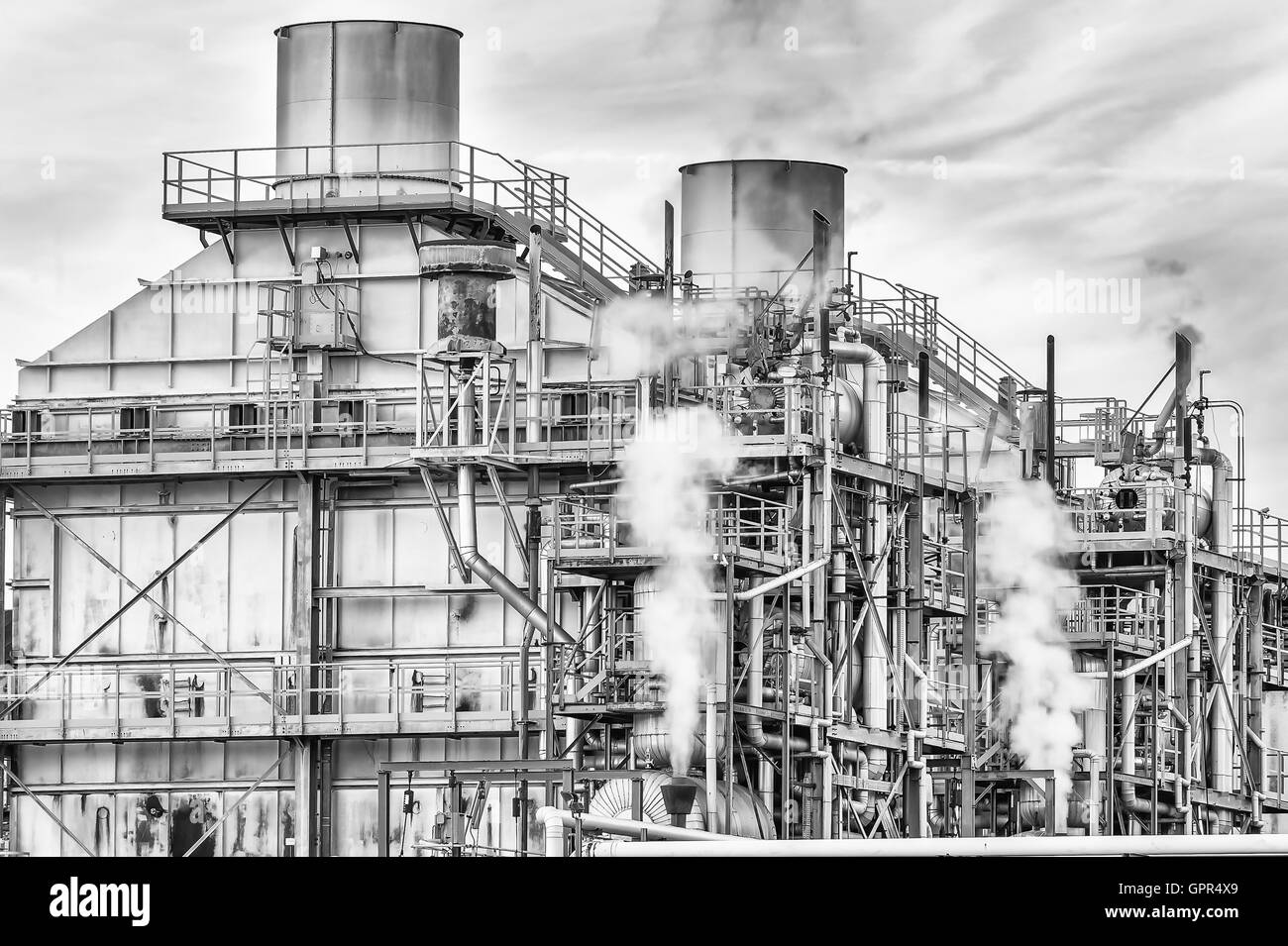 Impianto chimico di una fabbrica. Fumaioli ,le tubazioni e il serbatoio. In bianco e nero Foto Stock