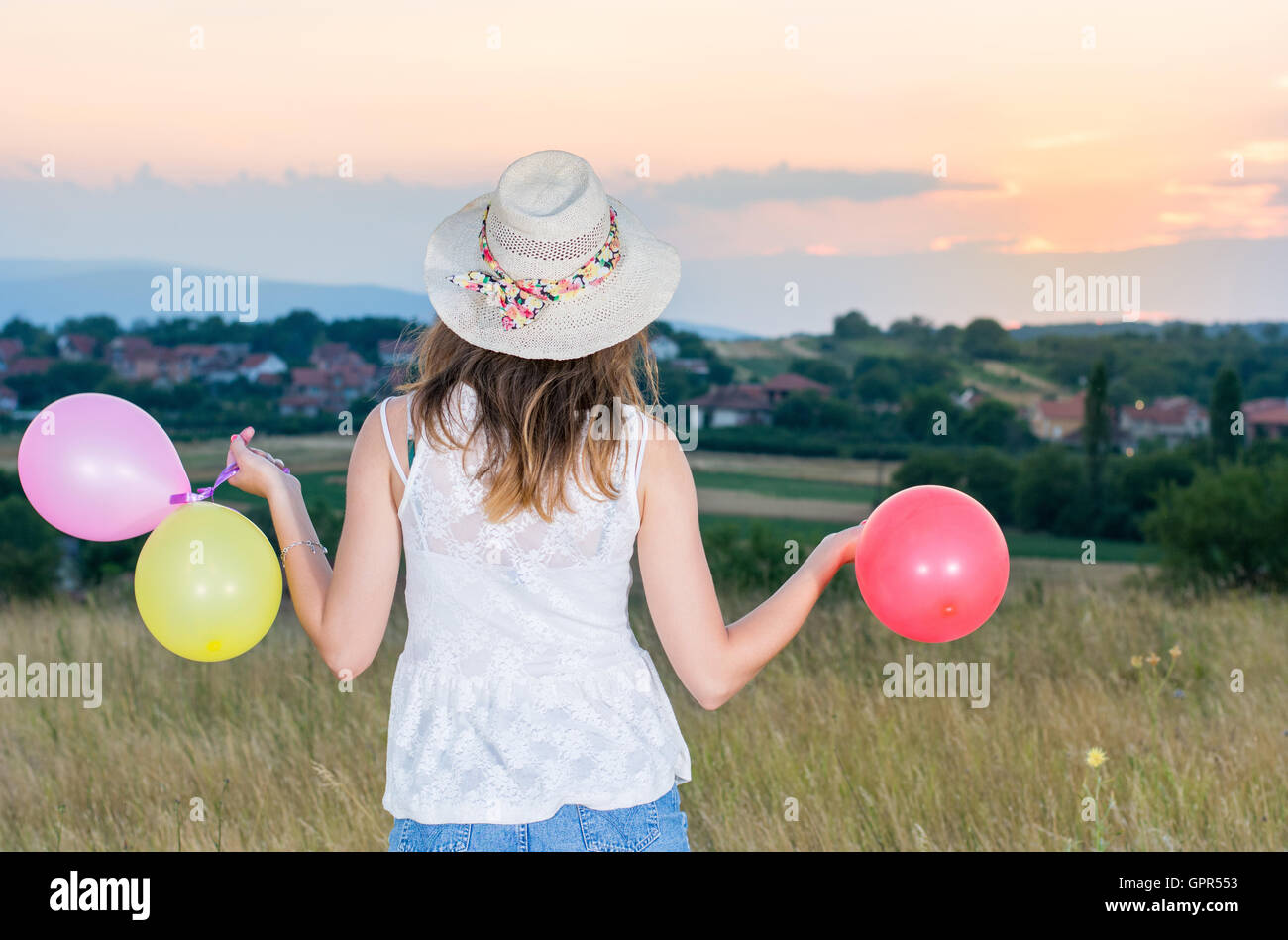 Giovane donna azienda palloncini e guardando il tramonto Foto Stock