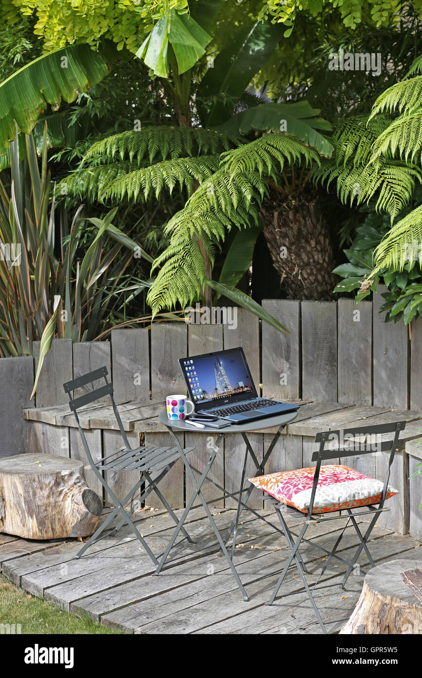 Lavorando da casa: un computer portatile, telefono intelligente e tazza da caffè su un tavolo da giardino in un ambiente urbano, UK giardino in un giorno d'estate. Foto Stock