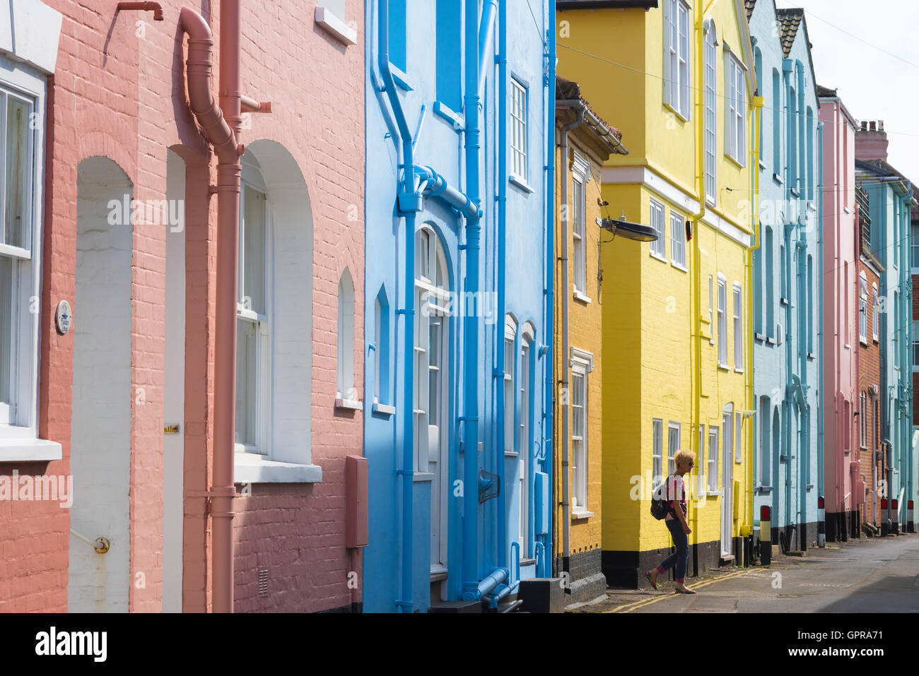 Viaggio in stile mare britannico, vista di una donna che indossa uno zaino che cammina tra le colorate case a schiera lungo il lungomare di Aldeburgh, Suffolk, Regno Unito. Foto Stock