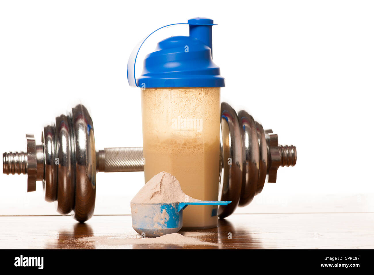 La proteina del siero di latte in polvere nella paletta, il manubrio, il metro a nastro e agitatore in plastica su sfondo di legno. Foto Stock