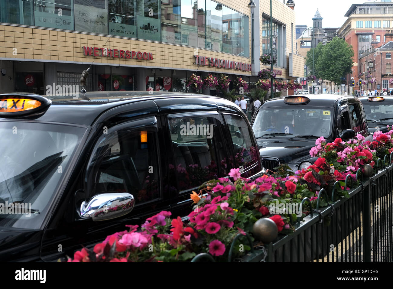 Una fila di taxi neri, taxi, con insegne luminose in attesa per i clienti su una trafficata High st Foto Stock