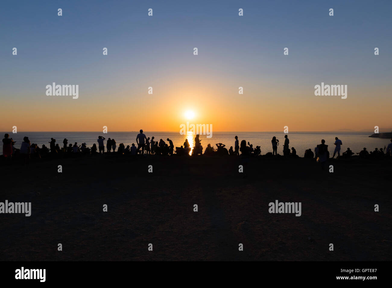Silhouette di persone a guardare il tramonto sul bordo della scogliera vicino Polente faro di Isola Bozcaada Foto Stock