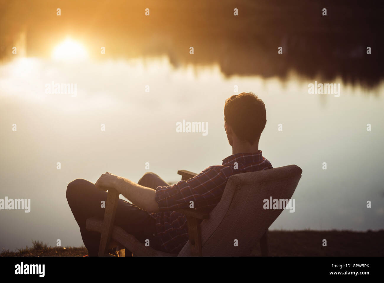 Uomo in sede presso la banca del lago guarda anche lontano su sunset Foto Stock