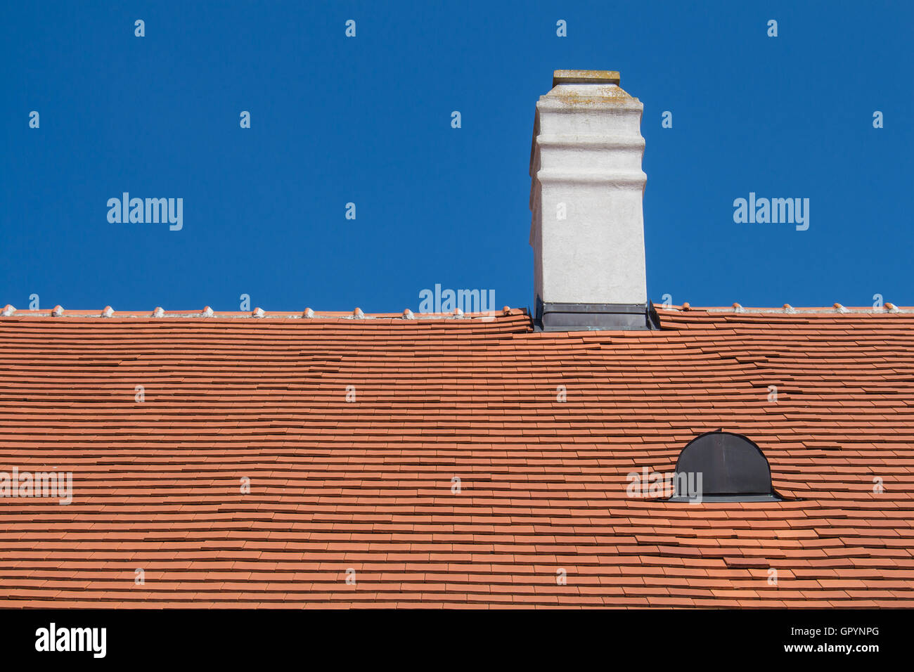 Rinnovato vecchio tetto arancione con un camino bianco e una finestra a tetto. Bright summer blue sky in background. Foto Stock