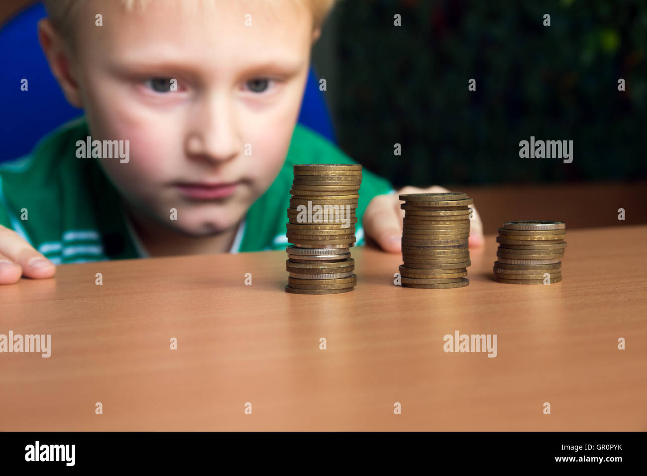 Happy Child (boy, capretto, teen) impilare le monete sul tavolo. I bambini ed il conteggio del concetto di denaro. Foto Stock