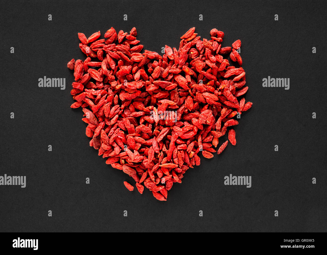 Materie essiccati goji bacche disposti in una forma di cuore su uno sfondo nero Foto Stock