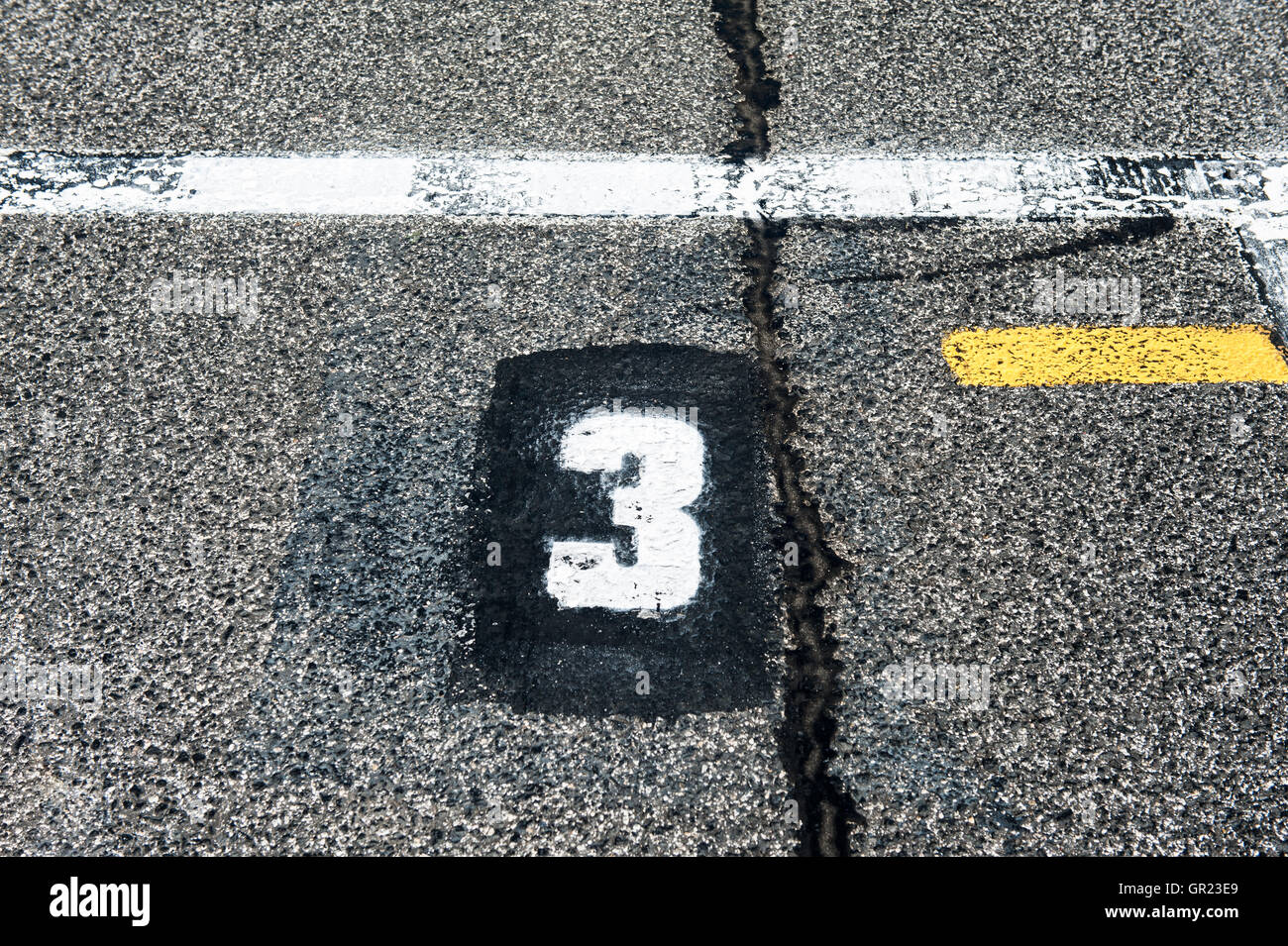 Numero tre è segno di posizione sullo speedway a partire via con la linea gialla e danneggiato vecchio asfalto Foto Stock