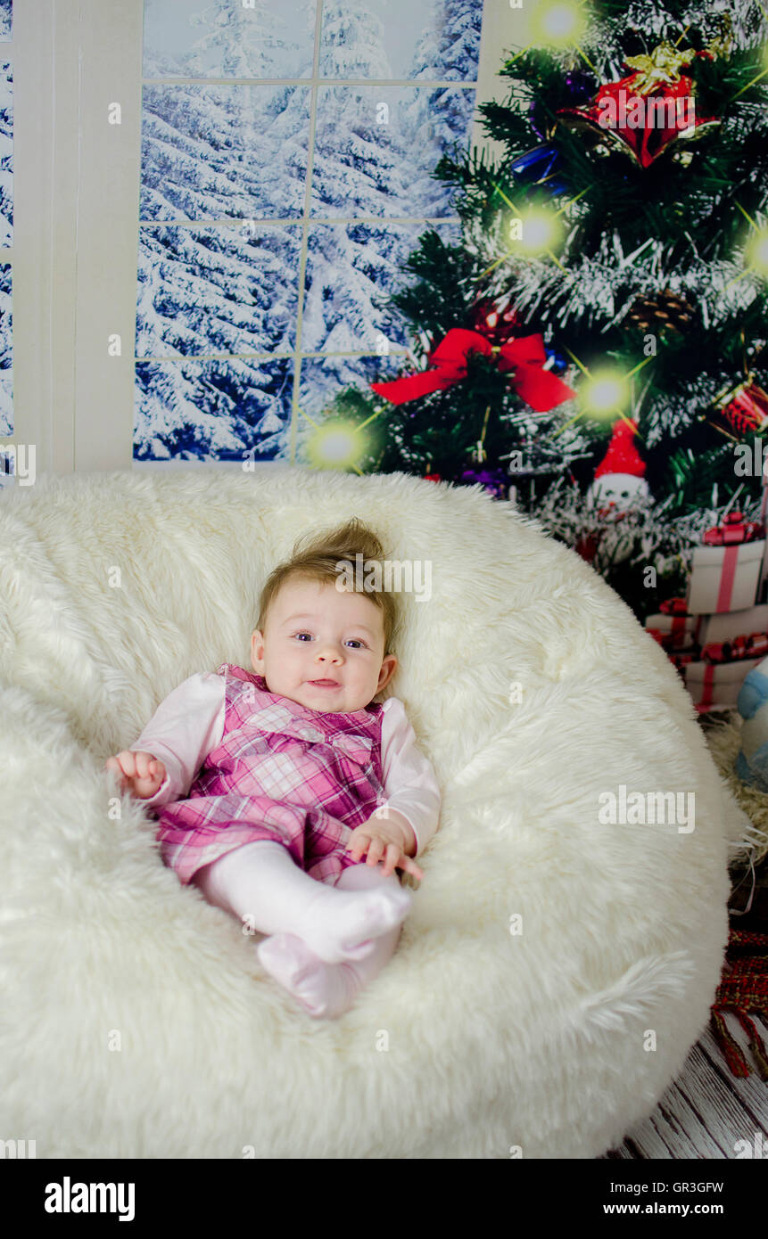 Baby girl godendo il suo primo Natale con un sacco di doni sotto albero di Natale Foto Stock