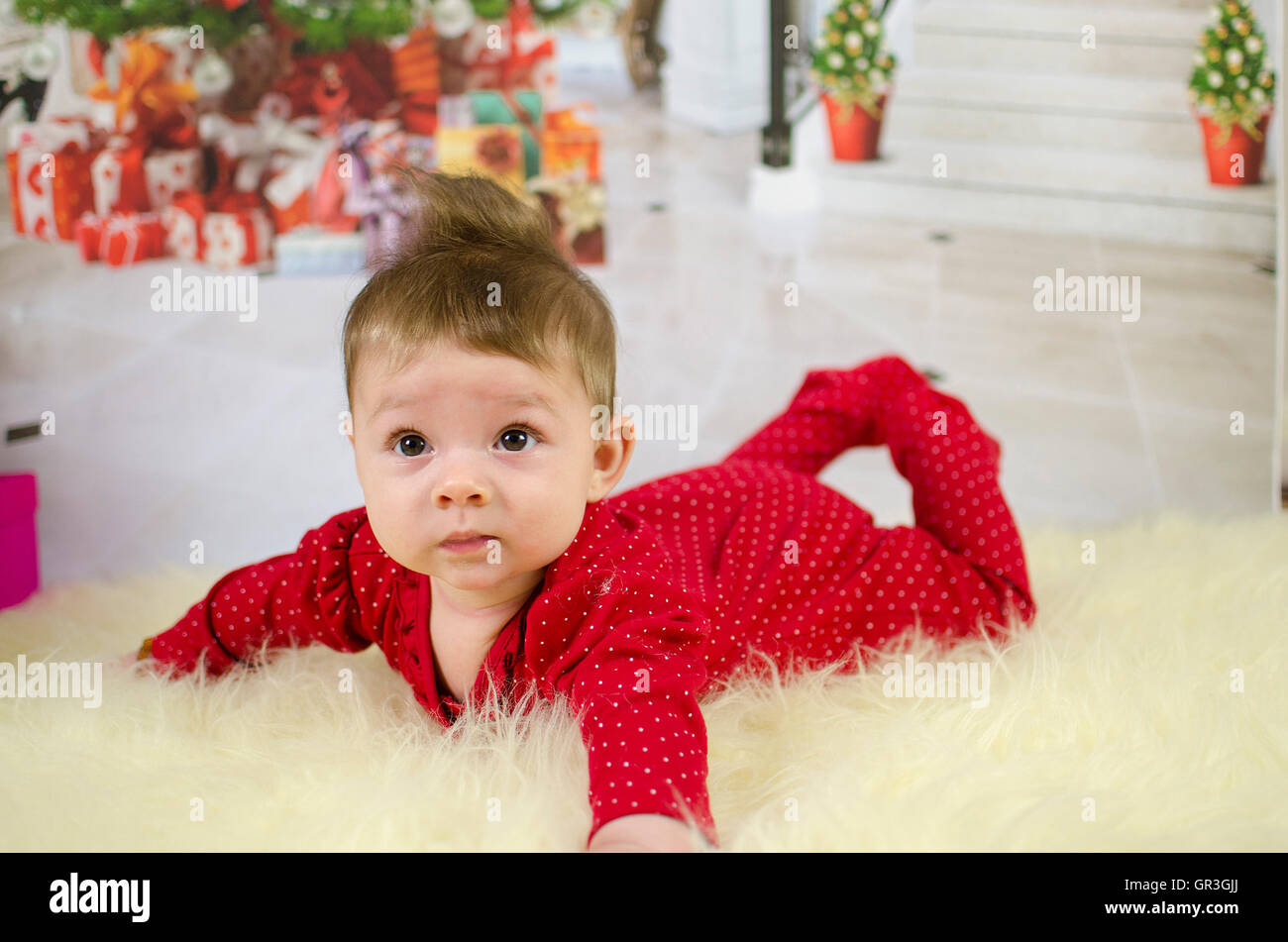 Baby girl godendo il suo primo Natale con un sacco di doni sotto albero di Natale Foto Stock