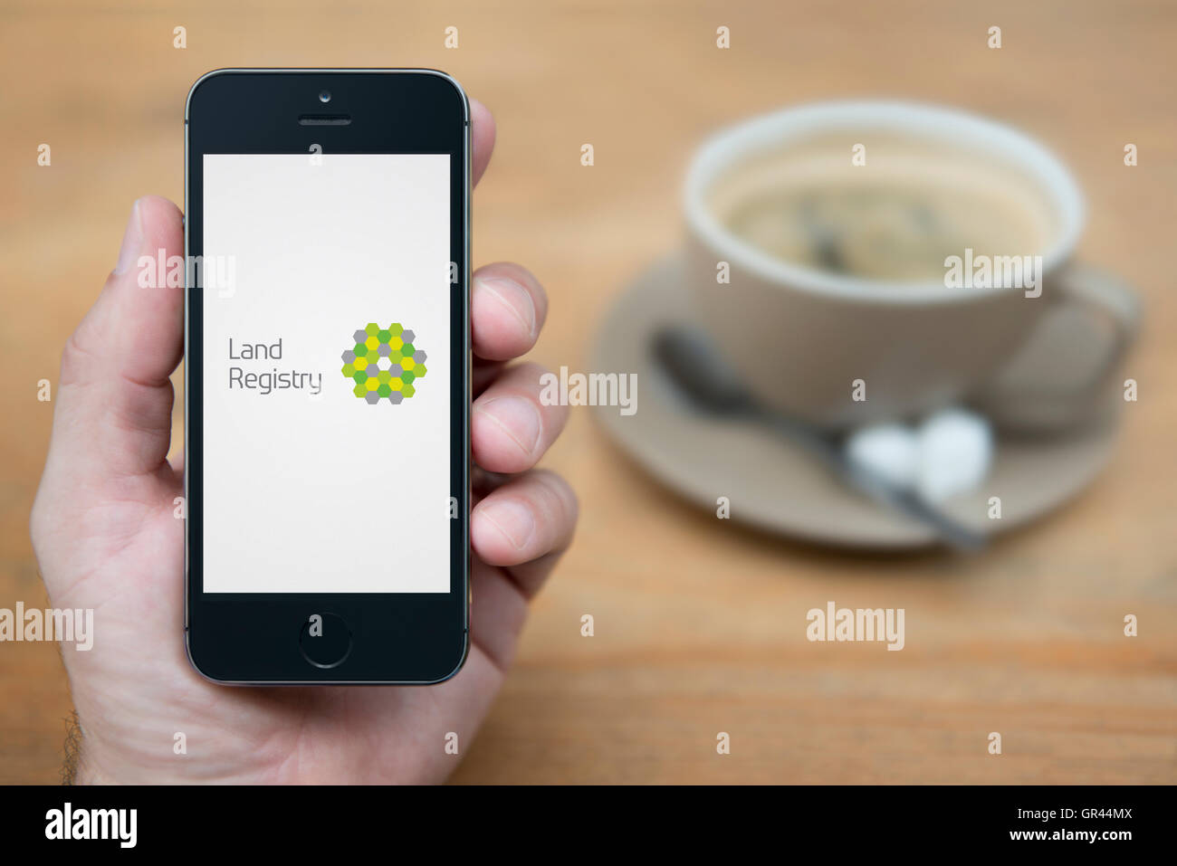 Un uomo guarda al suo iPhone che visualizza il governo britannico Catasto logo (solo uso editoriale). Foto Stock