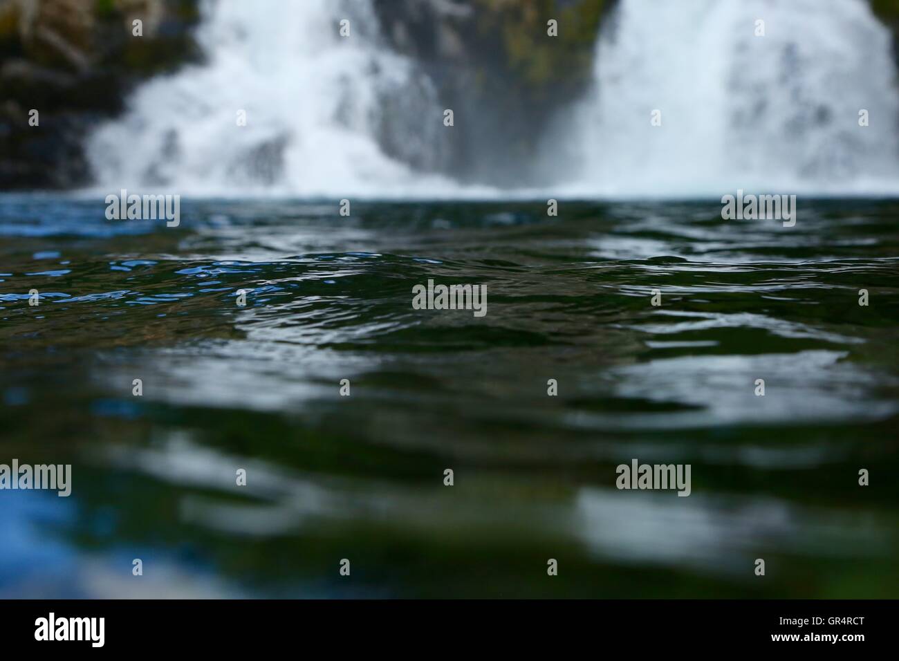 Messa a fuoco poco profonda su un ripple di acqua formando dalla corrente di imperversare cascate dietro di esso. Foto Stock