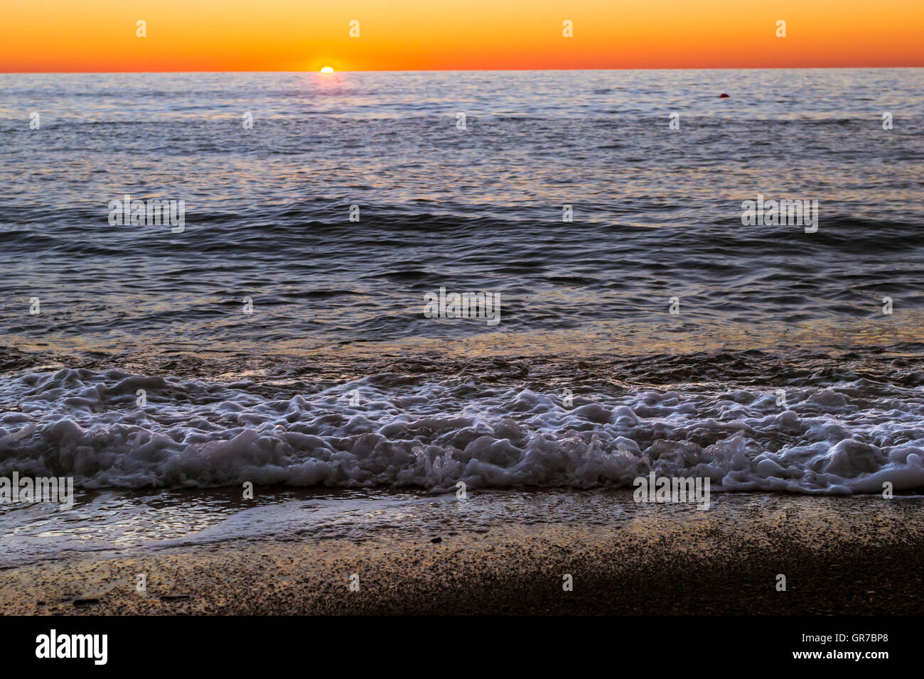 Schiuma di onde del mare si precipita a riva di ghiaia, riva della spiaggia è coperto di scintillanti pietre di sun. Brillante tramonto sulla costa del Mar Nero Foto Stock