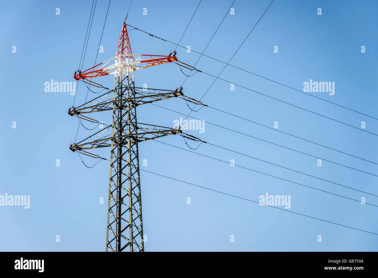 Montante d'angolo di una linea elettrica ad alta tensione con una punta rossa contro un cielo blu Foto Stock