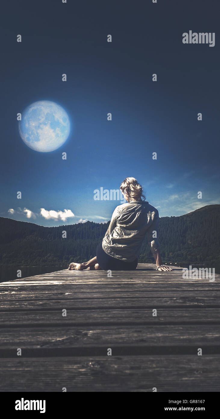 Giovane donna seduta e di pensiero su legno al chiaro di luna di luna piena Foto Stock