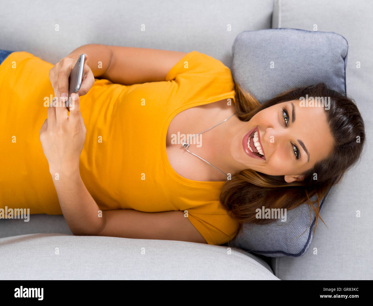 Vista dall'alto di una giovane e bella donna sdraiata su un divano e inviare messaggi di testo Foto Stock