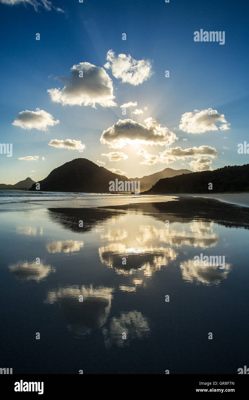 Bellissimo tramonto sull'oceano. Nuvole e sole che riflette la luce in acqua sulla spiaggia Foto Stock