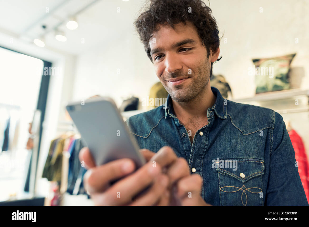 L'uomo sms sul cellulare in negozio di abbigliamento Foto Stock
