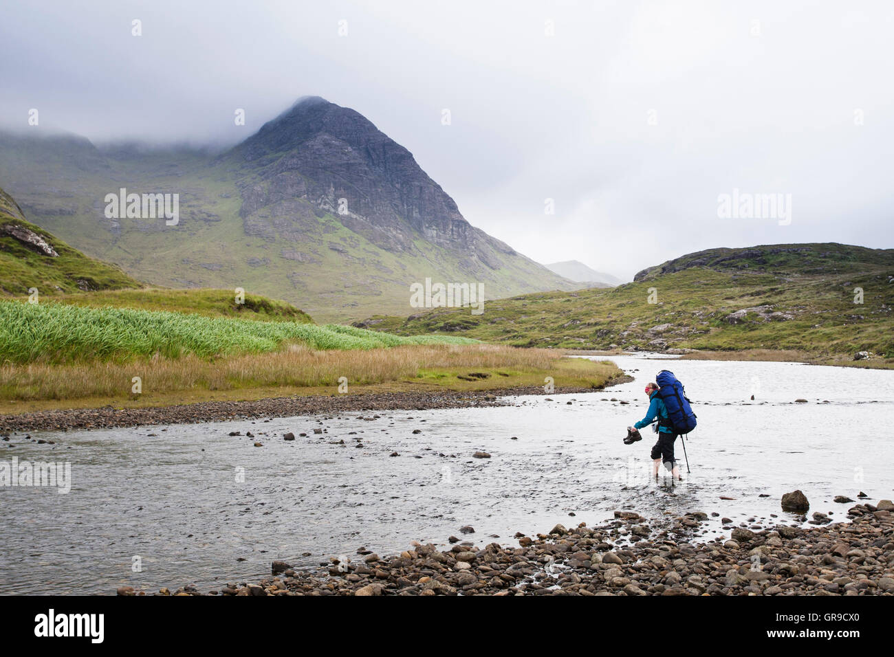 Donna con zaino Varcando il fiume (Abhainn Camas Fhionnairigh) con Sgurr Hain dietro, Camasunary, Isola di Skye, Scotland, Regno Unito Foto Stock