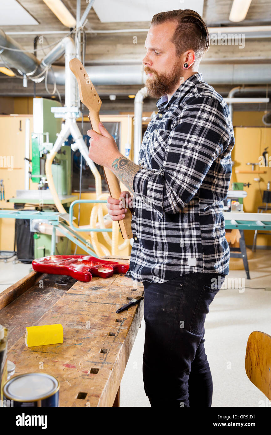 Carpenter ispeziona una chitarra in legno collo in officina Foto Stock