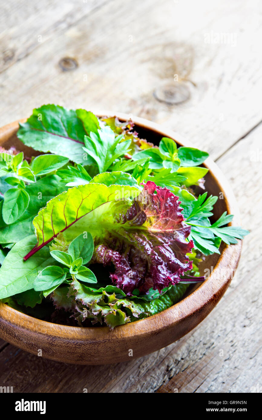 Organico fresco verde insalata mista lascia su legno rustico sfondo con spazio di copia Foto Stock