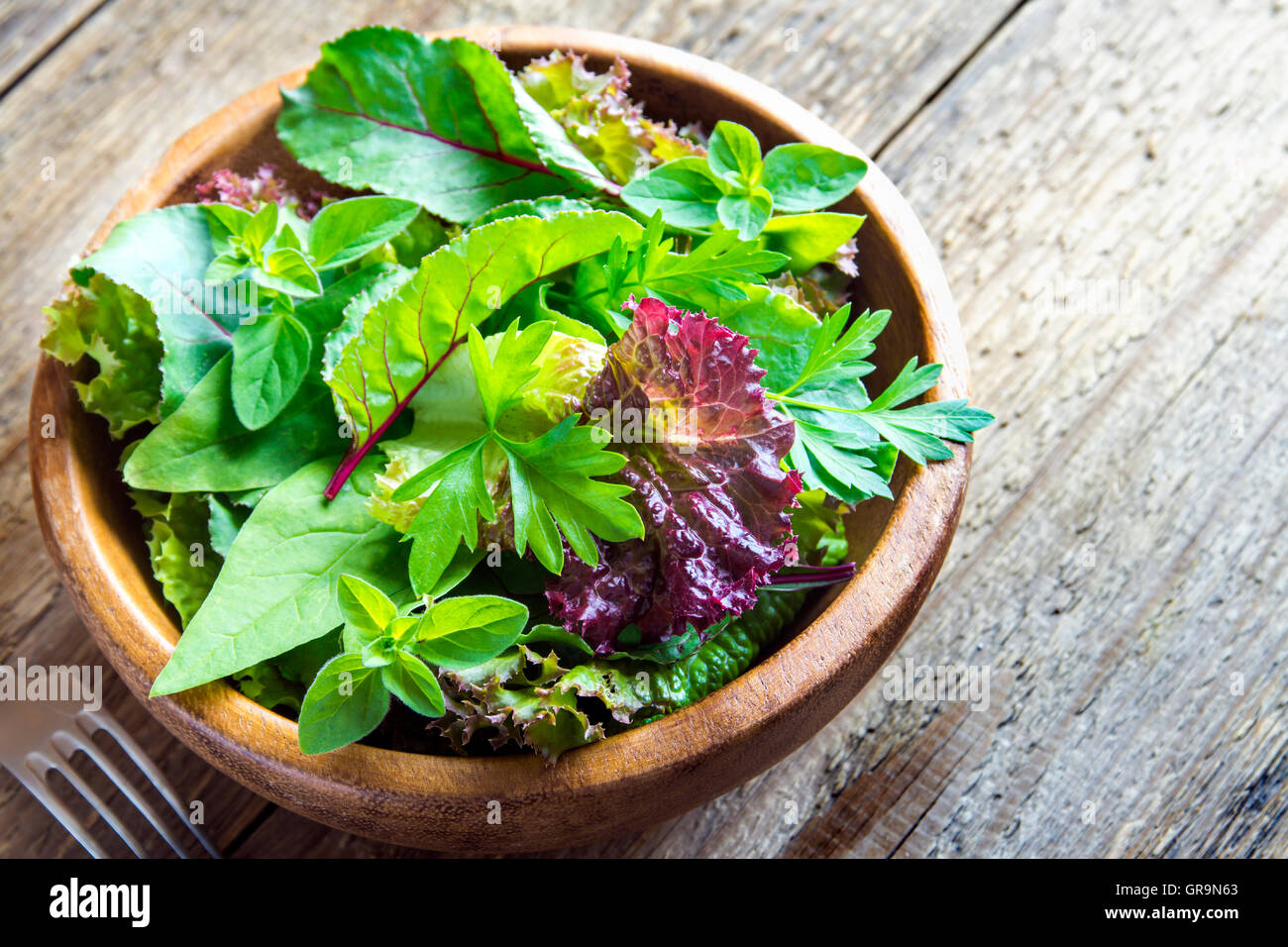 Organico fresco verde insalata mista lascia su legno rustico sfondo con spazio di copia Foto Stock