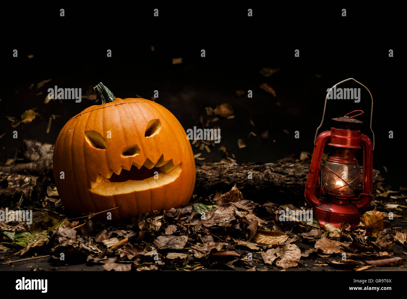 Zucca di Halloween con lanterna rossa su legno fogliame. Impostazione scuro e lo sfondo. Studio shot. Foto Stock