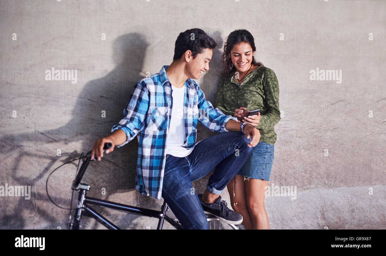 Giovane adolescente con biciclette BMX texting con un telefono cellulare in corrispondenza della parete Foto Stock