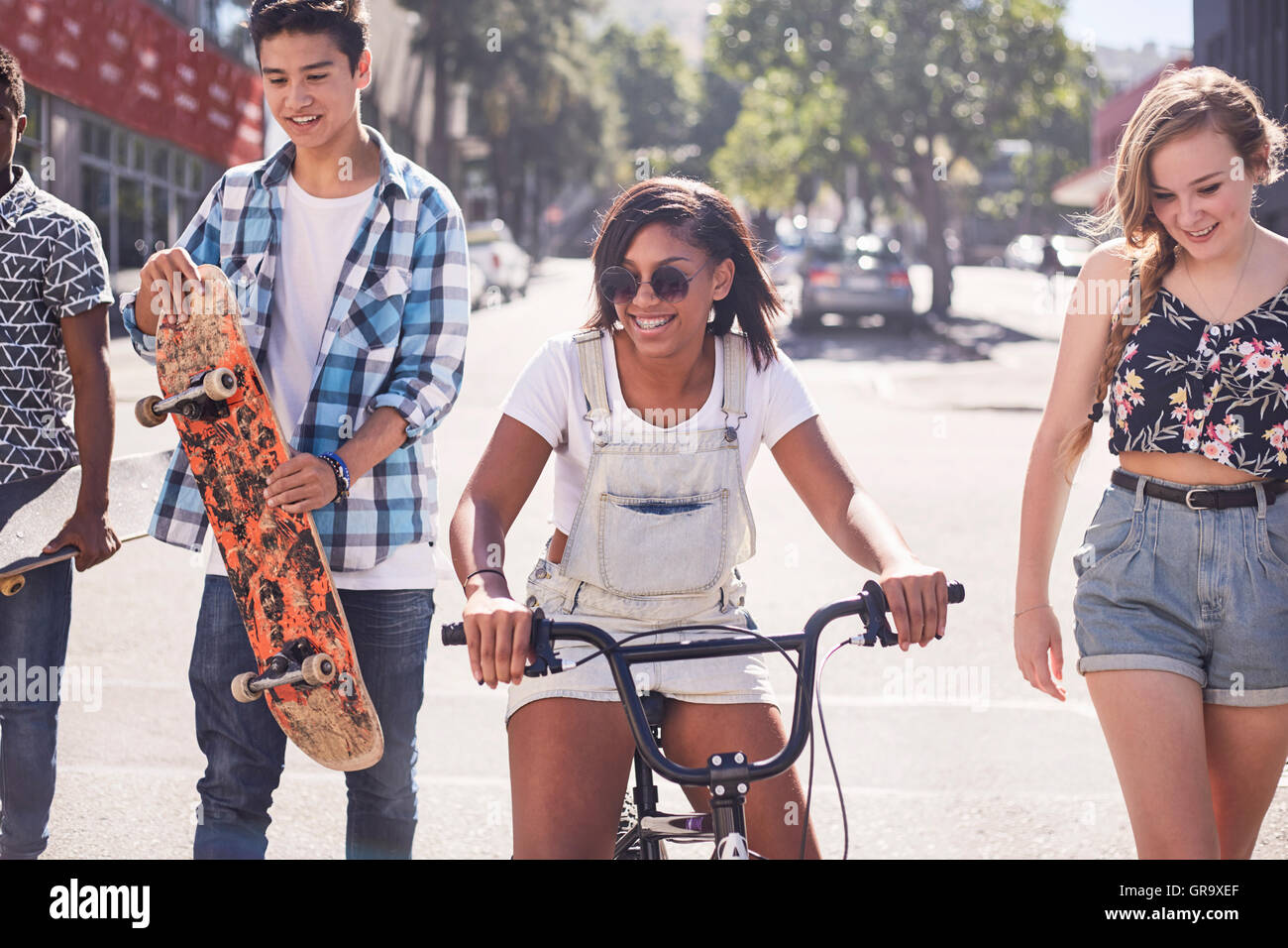 Amici di adolescenti con lo skateboard e biciclette BMX sulla soleggiata strada urbana Foto Stock