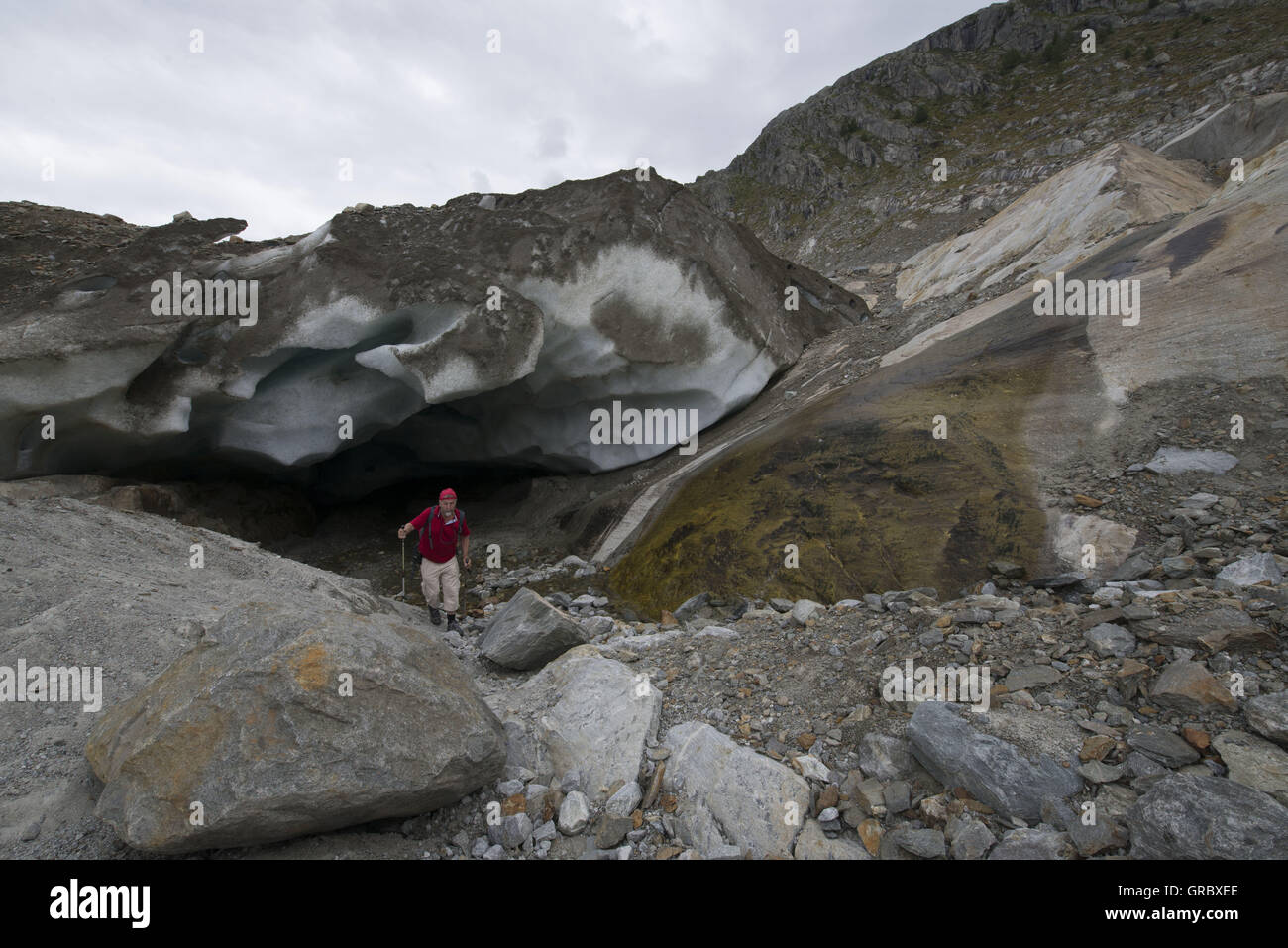 Escursionista presso l'entrata di una caverna sul ghiacciaio del grande ghiacciaio di Aletsch, massi in primo piano Foto Stock