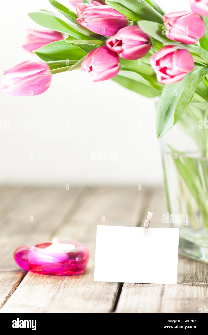 Viola i tulipani in un vaso accanto a un vecchio tavolo in legno candela brucia Foto Stock