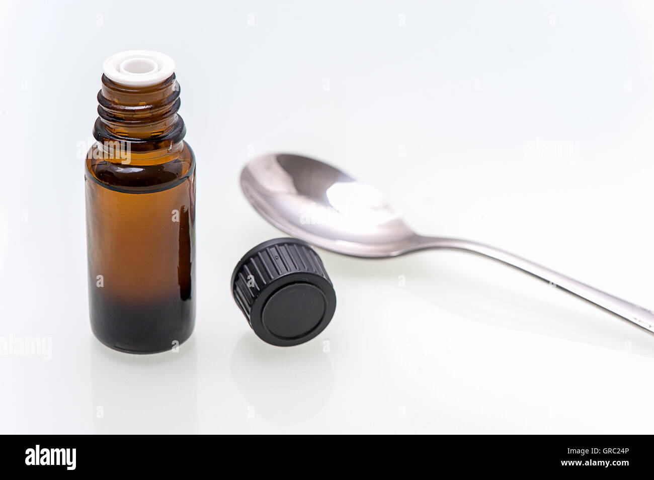 Bottiglia marrone con la medicina su sfondo bianco è accanto al coperchio e un cucchiaio Foto Stock