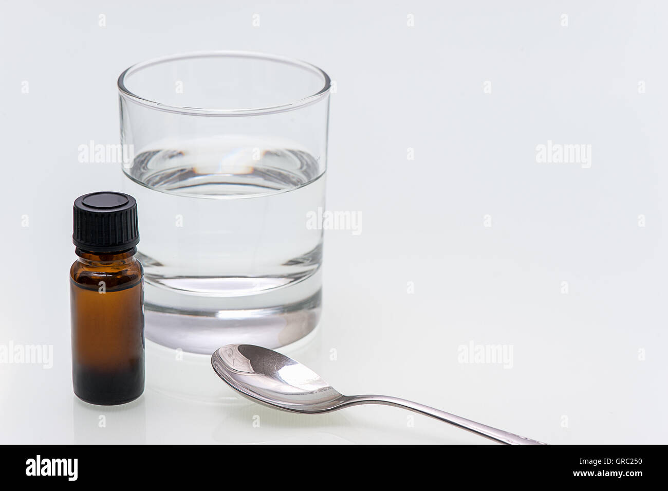 Bottiglia marrone con la medicina su sfondo bianco è accanto al coperchio e un cucchiaio Foto Stock