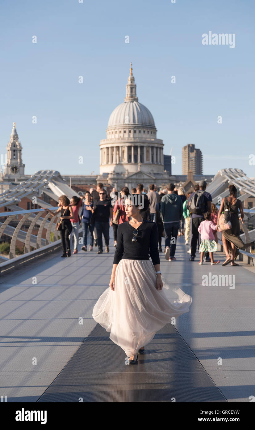 Donna in abito fluente attraversando a piedi il Millenium Bridge di distanza dalla Cattedrale di San Paolo a Londra, Inghilterra. Foto Stock