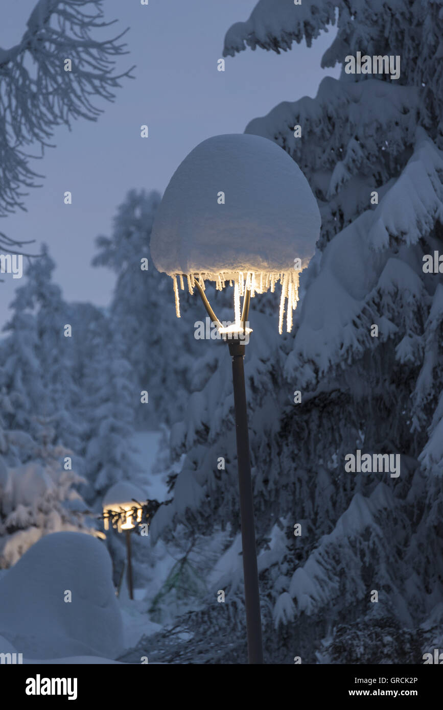 Dawn, profondamente nevicato in passa-foreste con brillanti lampioni. Lampioni Icicled e coperto con grandi Snowcaps Foto Stock