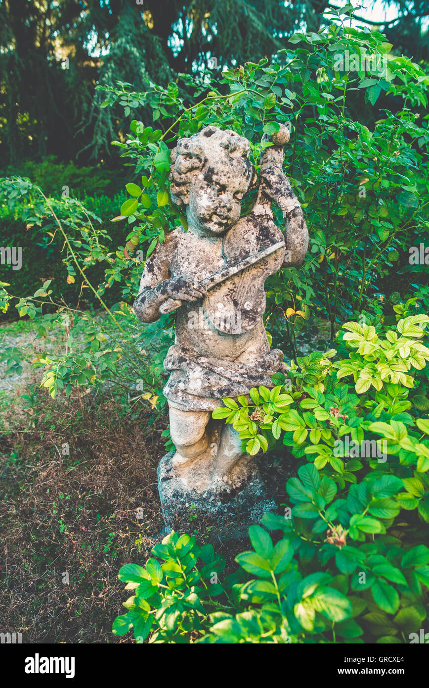 Statua di Pietra di un cherubino suona il violino in un giardino Foto Stock