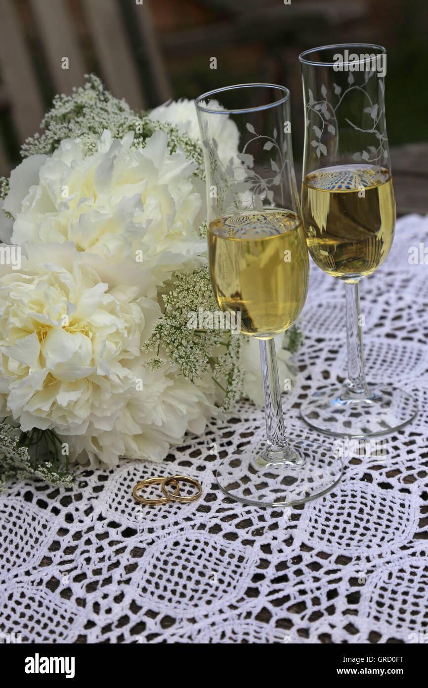 Simboli di nozze, nozze bianco fiori e Golden gli anelli di nozze, due bicchieri di champagne Foto Stock