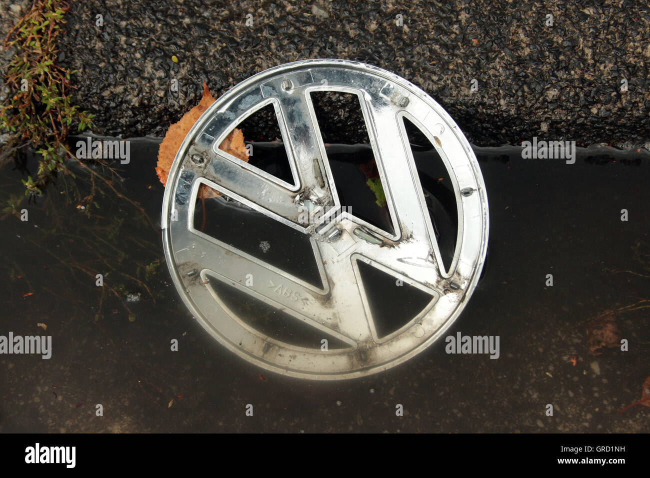 Crisi a Vw Volkswagen segno giacente in una pozza in corrispondenza di un cordolo Foto Stock