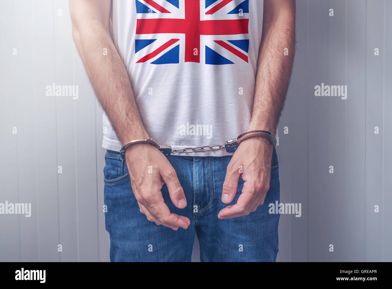 Arrestato uomo con ammanettato mani indossando camicia con Regno Unito bandiera. Irriconoscibile la persona di sesso maschile in jeans con manette detenuto mi Foto Stock