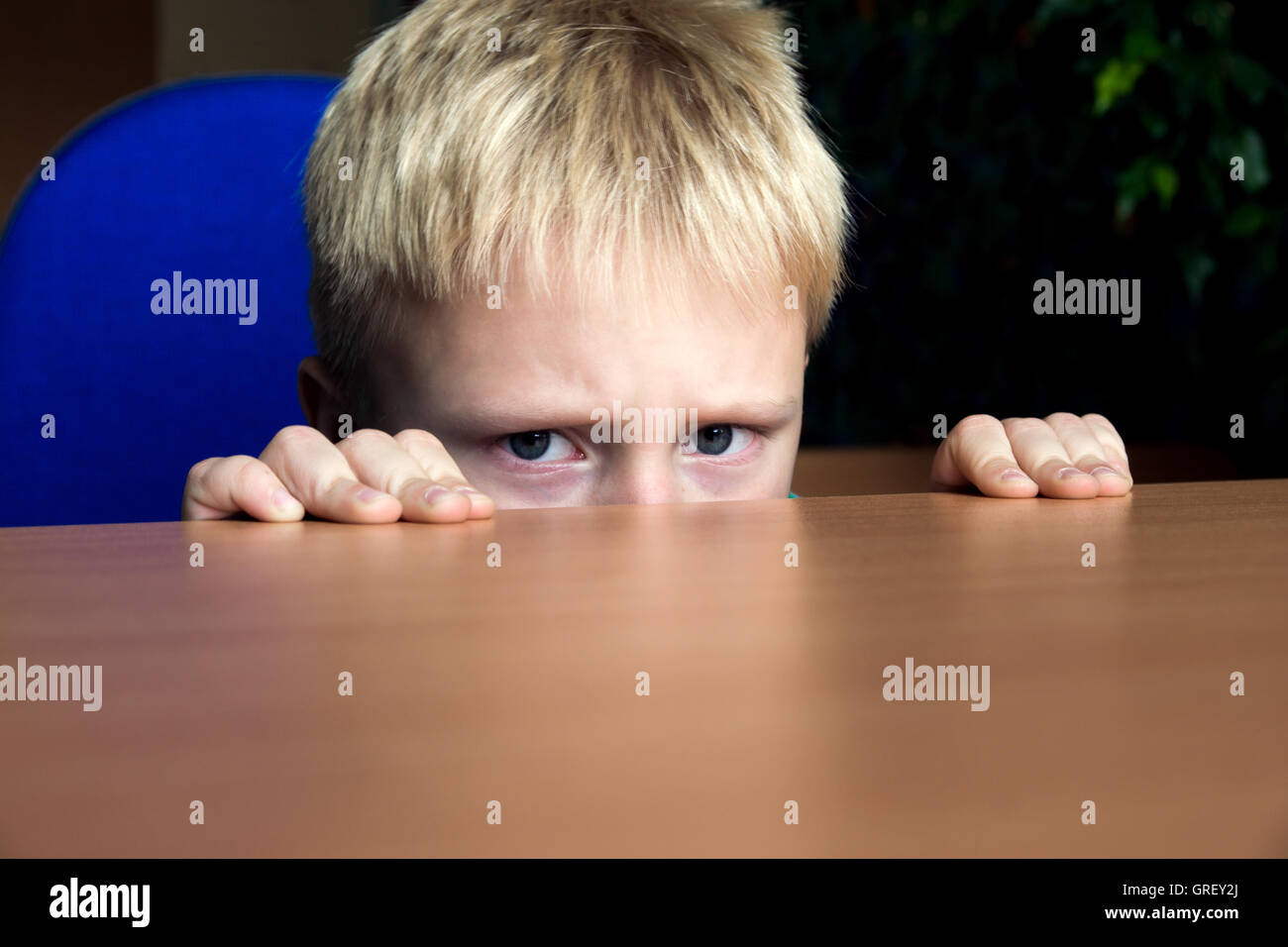 Triste sconvolto infelice ragazzo ragazzo nascosto sotto il tavolo Foto Stock