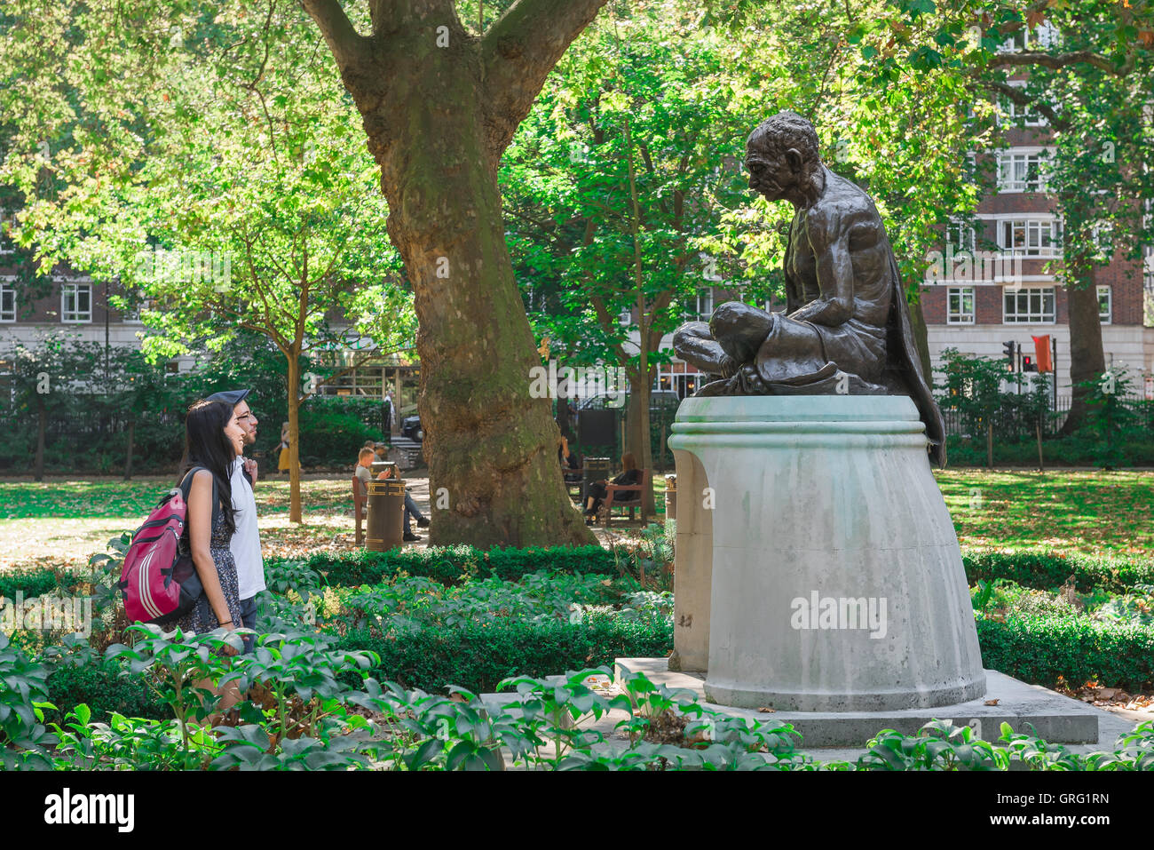London Square Gandhi, vista di una giovane coppia guardando la statua del Mahatma Gandhi in Tavistock Square park su una mattina d'estate, Bloomsbury, UK. Foto Stock