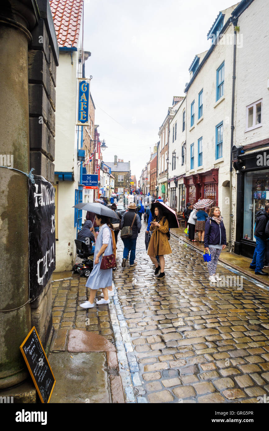 Gruppo di turisti orientali e varie altre persone su Church Street, in un giorno di gran pioggia. a Whitby Foto Stock