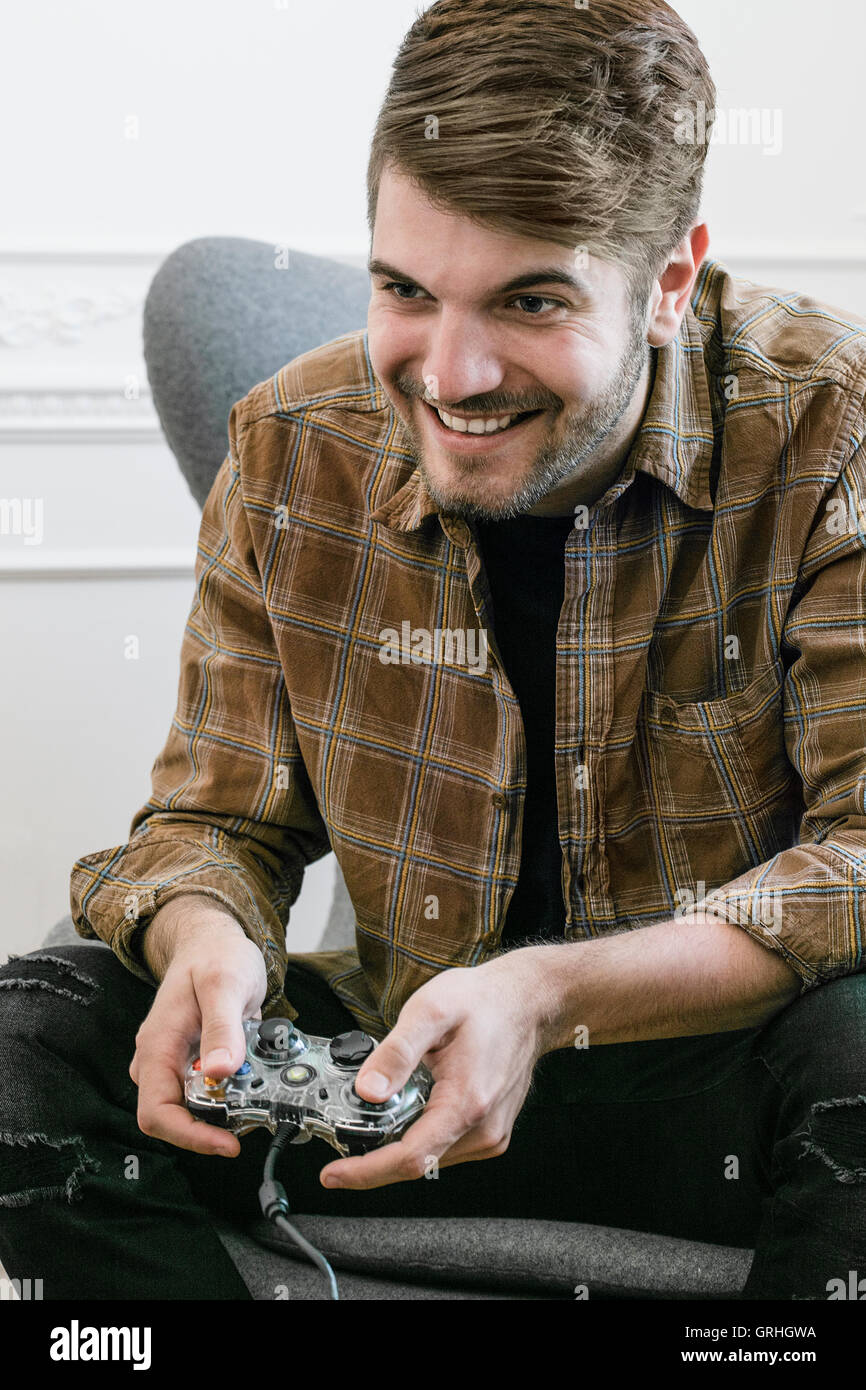 Un giovane dai capelli scuri uomo si inclina in avanti nella sua sedia mentre si tiene un controller di gioco. Foto Stock