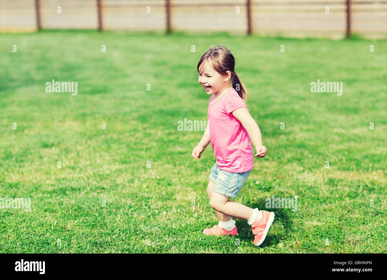 Felice bambina in esecuzione sul verde del campo estivo Foto Stock