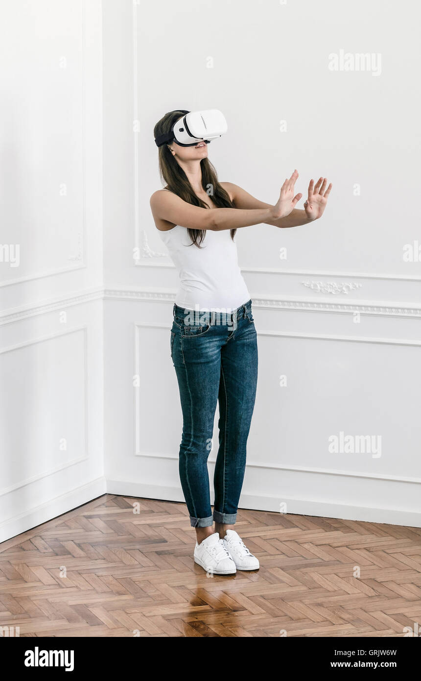 Una giovane donna si trova in un appartamento sensazione attorno a sé indossando una realtà virtuale auricolare Foto Stock